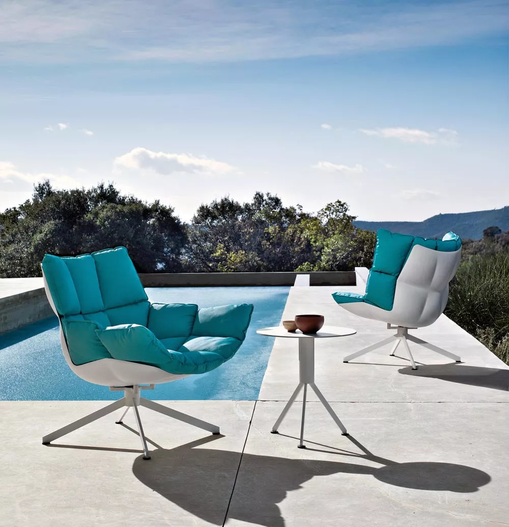 Zwei B&B Italia Husk Outdoor Loungesessel in Türkis stehen auf einer Terrasse neben einem Pool mit einem kleinen Tisch dazwischen