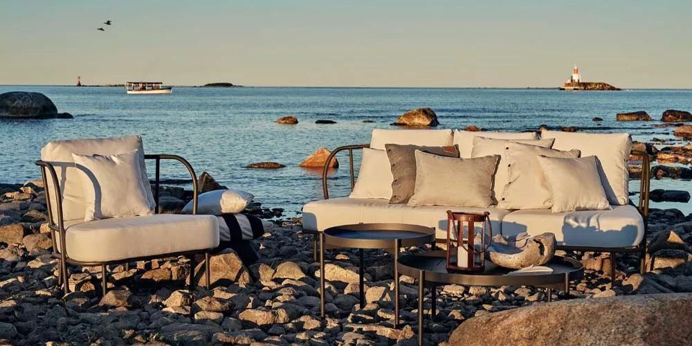 Skargaarden Saltoe Outdoor-Möbelset in Weiß auf einem felsigen Strand mit Meerblick bei Sonnenuntergang, stimmungsvolle Atmosphäre.