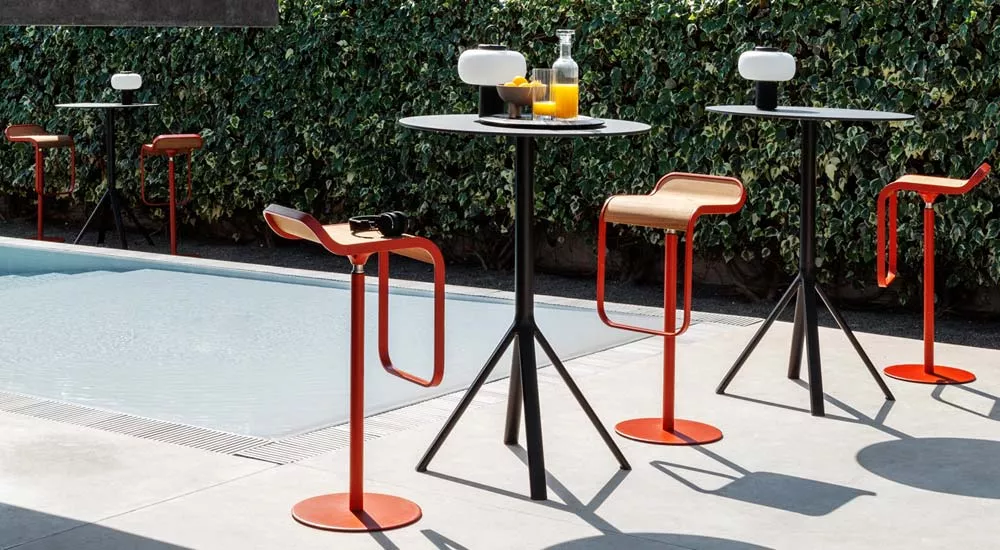 Lapalma LEM Outdoor Barhocker in Rot und Schwarz vor einer Hecke am Pool, mit Tisch und Getränken, in sommerlicher Atmosphäre.