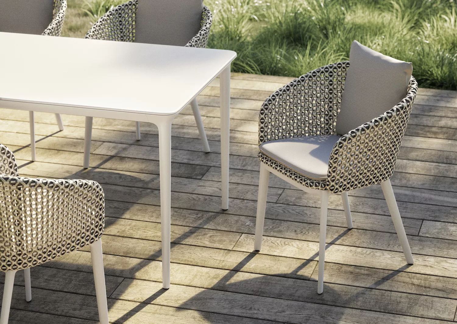 DEDON BELLMONDE Gartenmöbel auf einer Holzterrasse mit grünem Rasen im Hintergrund vier Stühle und ein Tisch in einer entspannten Atmosphäre