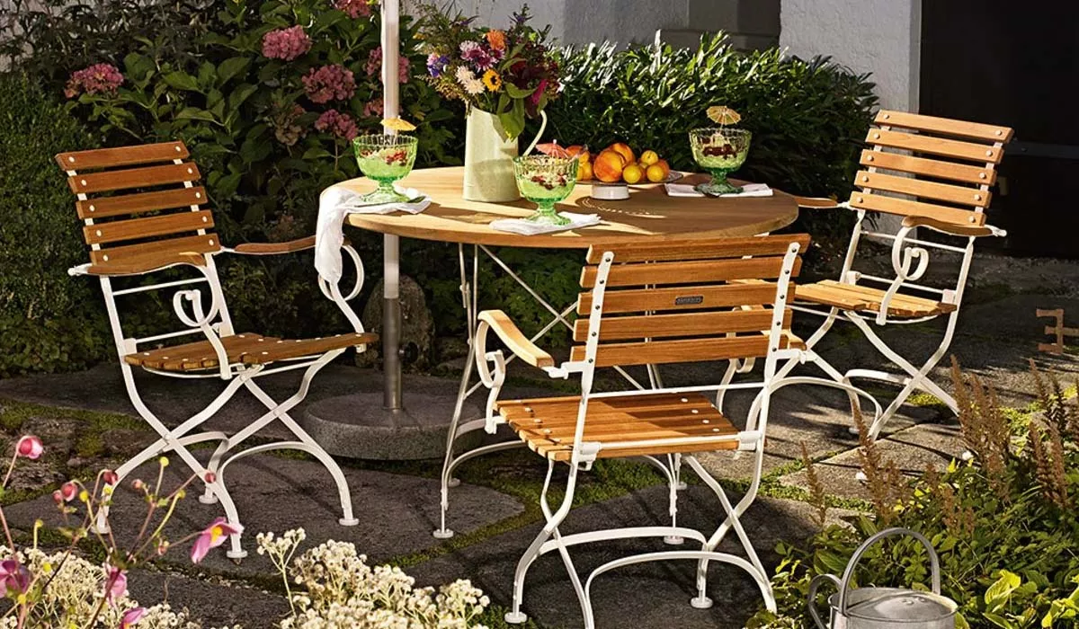 Weißhäupl Stuhl, Holz und Metall, braun und weiß, im Garten auf Steinboden neben einem runden Tisch mit Blumen und Obst.