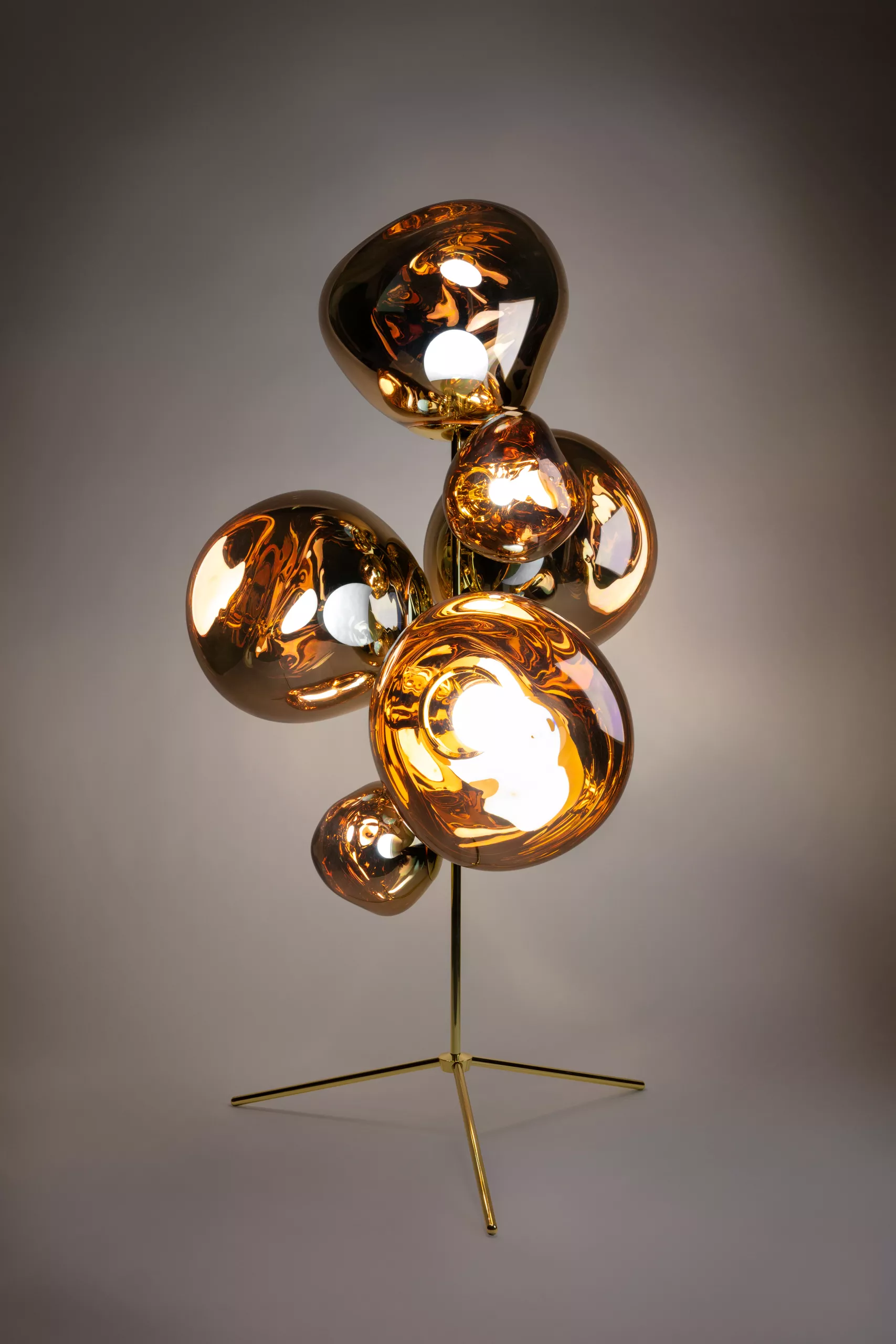 Tom Dixon Standkronleuchter MELT in Gold auf grauem Hintergrund, stimmungsvolle Beleuchtung, ideal für festliche Dekorationen.