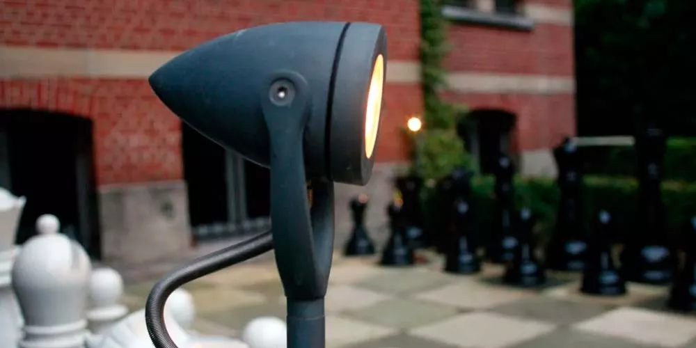 Royal Botania Bullet Gartenleuchte in Schwarz, stimmungsvolles Bild im Außenbereich vor einer Backsteinmauer und Schachfiguren.