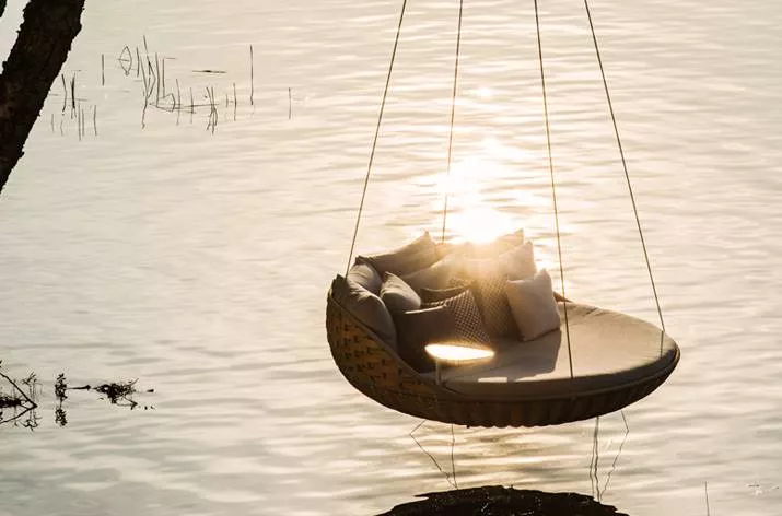 Dedon Swingrest Hanging Lounger hängt über einem ruhigen See im Sonnenuntergang mit mehreren Kissen auf der Sitzfläche Moodbild