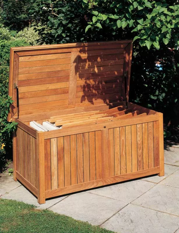 Barlow Tyrie Aufbewahrungskiste, 150 cm, aus Holz, geöffnet im Garten auf Steinboden, umgeben von grünen Pflanzen.