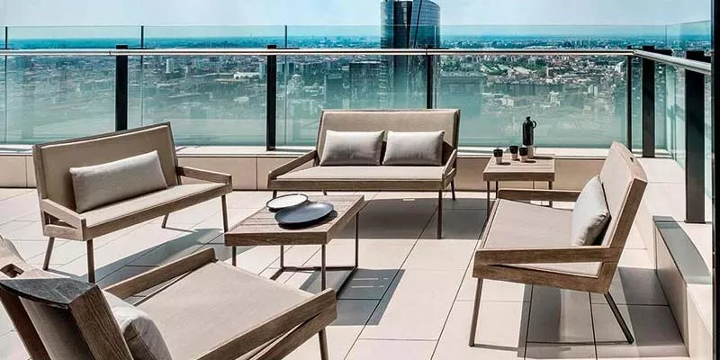 Ethimo Allaperto Urban Outdoor Loungegruppe in Beige auf einer modernen Dachterrasse mit Glasgeländer und Stadtblick.