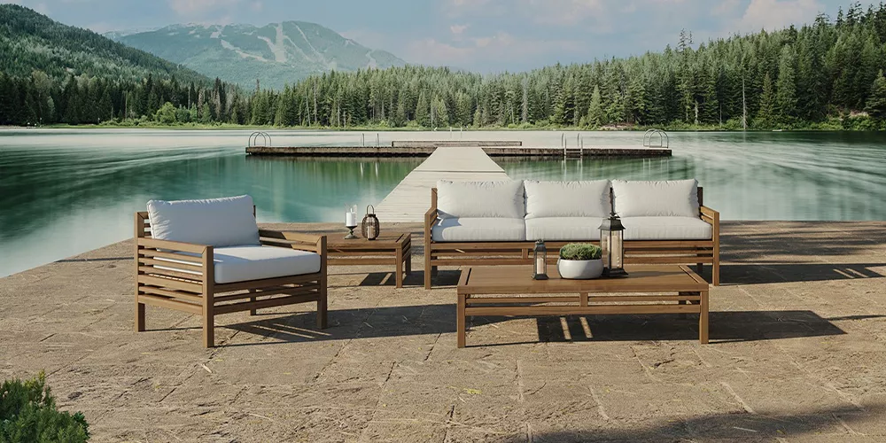 Cubic Outdoor Living Set in Naturholzoptik mit weißen Polstern auf einer Terrasse am See vor bewaldeter Bergkulisse bei Sonnenschein.