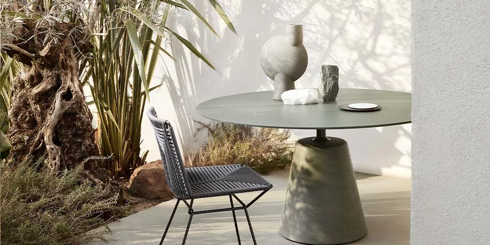 MDF Italia Rock Table in Grün, runder Tisch im Freien, umgeben von Pflanzen, mit dekorativen Vasen und einem Stuhl auf einer Terrasse.