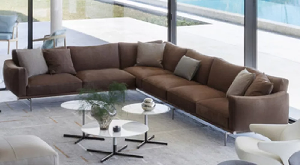 Braunes Poltrona Frau Happy Jack Sofa in modernem Wohnzimmer mit großen Fenstern und Blick auf den Pool, umgeben von Beistelltischen.