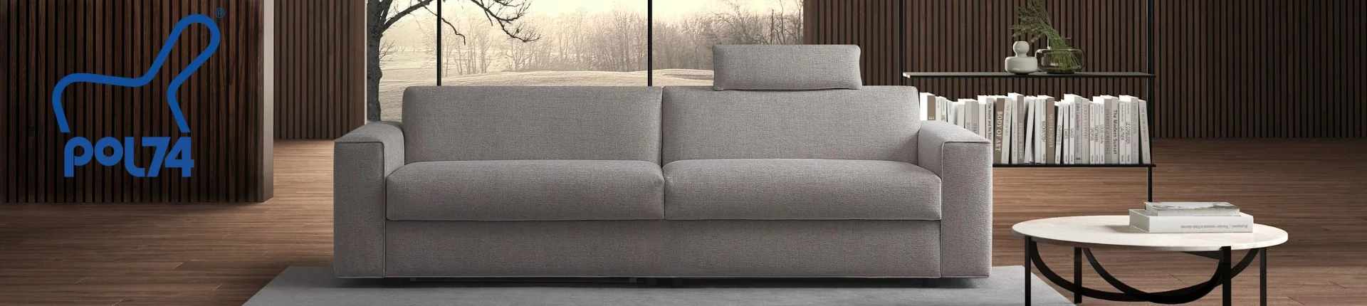 Graues Pol74-Sofa in modernem Wohnzimmer mit Holzvertäfelung und Bücherregal, Logo links, stimmungsvolle Winterlandschaft im Hintergrund.