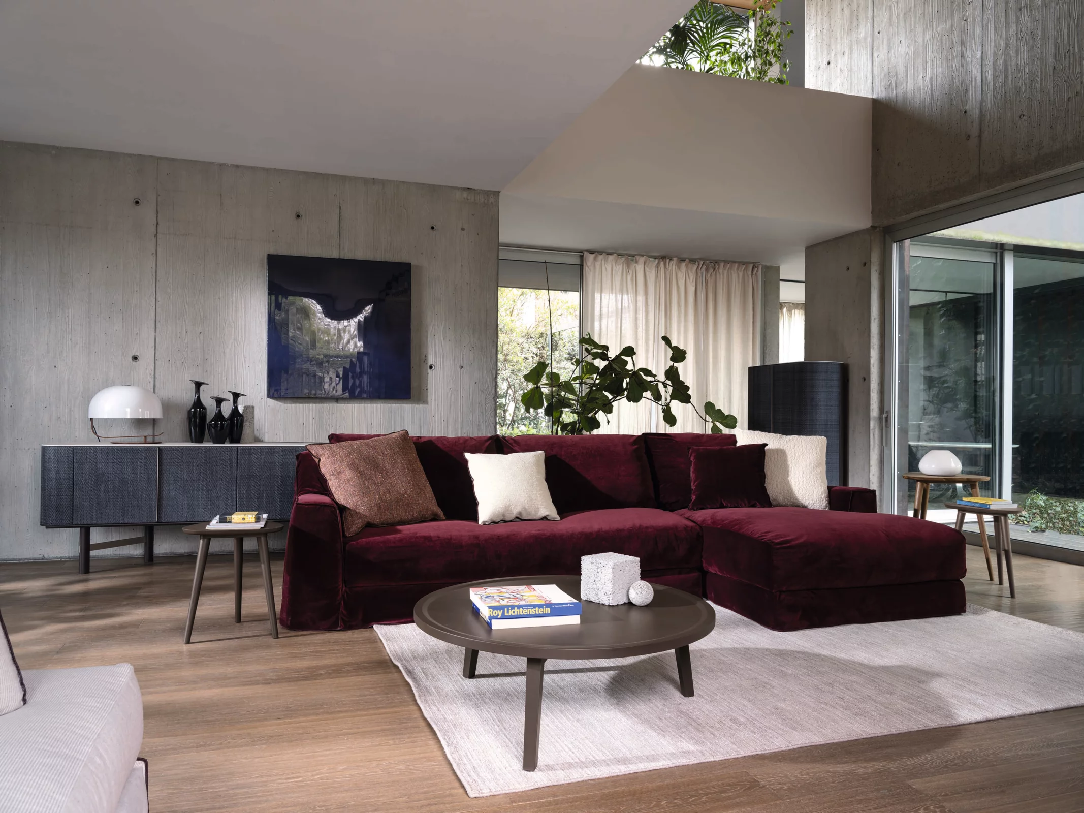 Ein Wohnzimmer mit einem Gervasoni Sofa in dunkelrotem Samt ein Couchtisch mit Büchern und Dekorationen und eine moderne Einrichtung im Hintergrund.