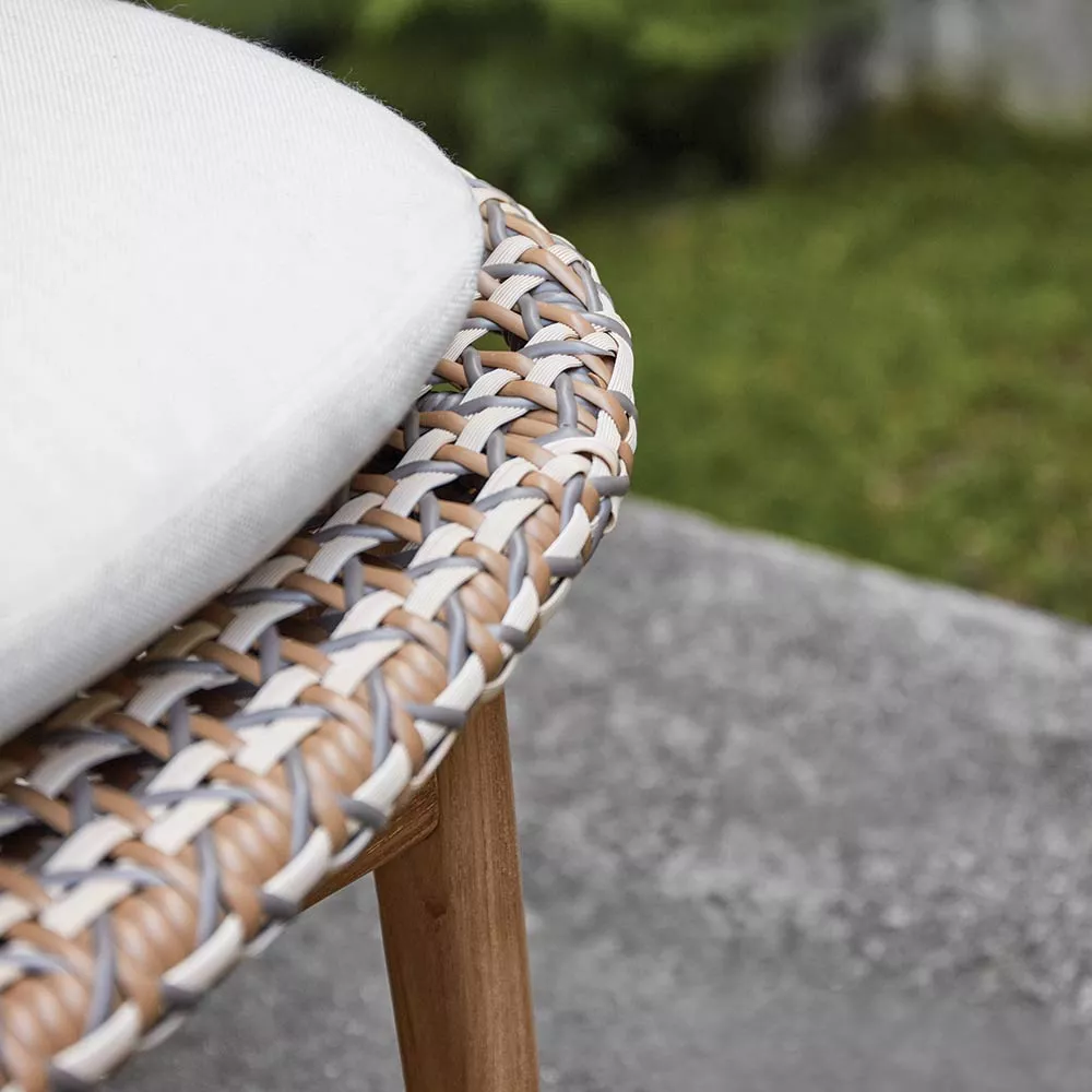 Gloster Kay Schaukelsessel in Beige und Holzoptik, Detailansicht des Geflechts auf grauem Steinboden im Garten.