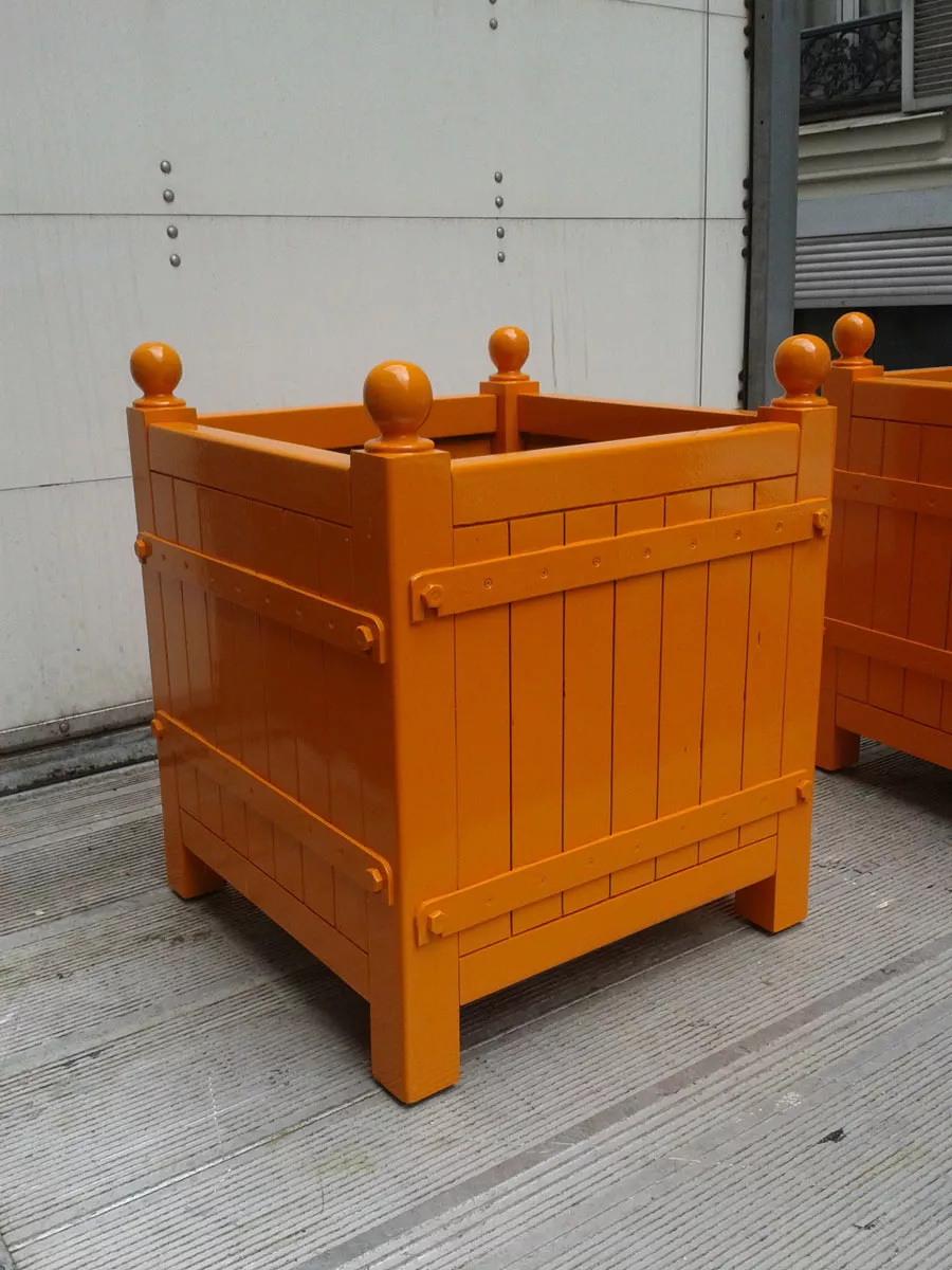 Orangerie Pflanzkübel aus lackiertem Akazienholz in leuchtendem Orange auf einer Terrasse stehend