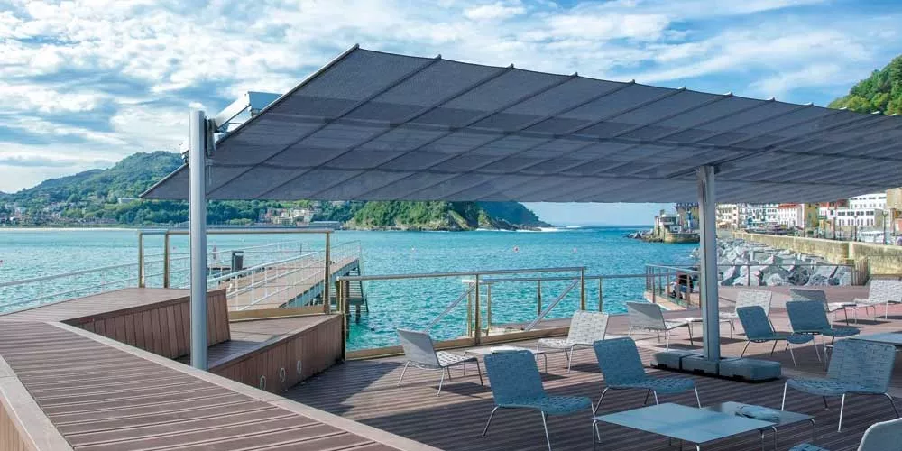 Großer FIM Flexy Sonnenschirm in Grau auf einer Terrasse mit Meerblick, umgeben von modernen Sitzmöbeln und Holzdeck.
