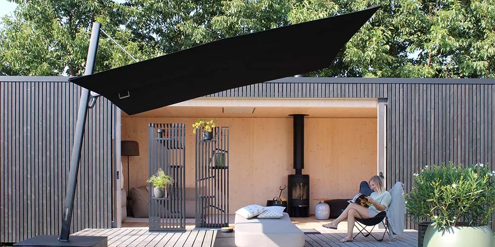 Ein schwarzes Sonnensegel von Spactraux über einer modernen Terrasse mit Holzverkleidung und entspannter Person im Hintergrund.