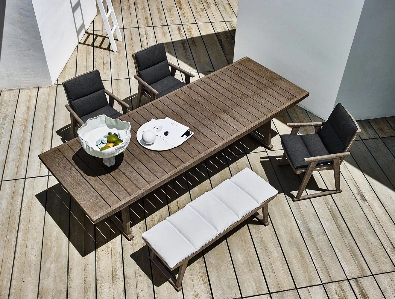 B&B Italia Gio Gartentisch 280 cm mit vier Stühlen und einer Bank auf einer Terrasse mit Dekorationselementen wie Schalen und Zeitschriften