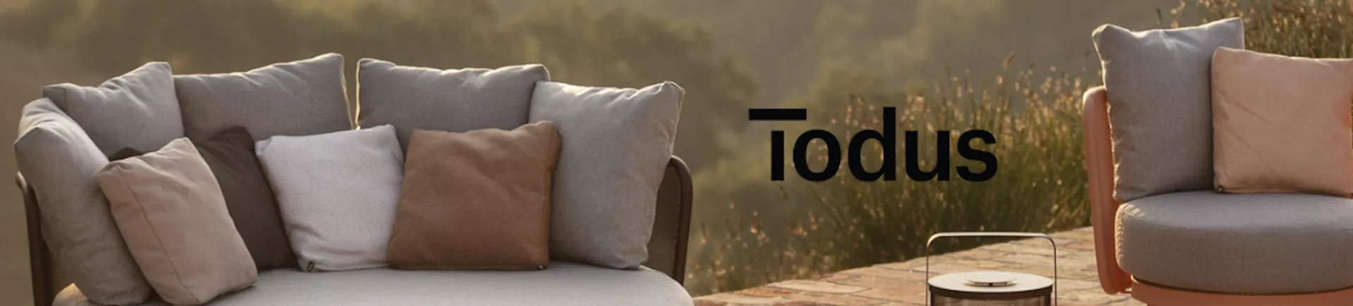 Todus Outdoor-Möbel in Erdtönen auf einer Terrasse mit Naturhintergrund bei Sonnenuntergang.