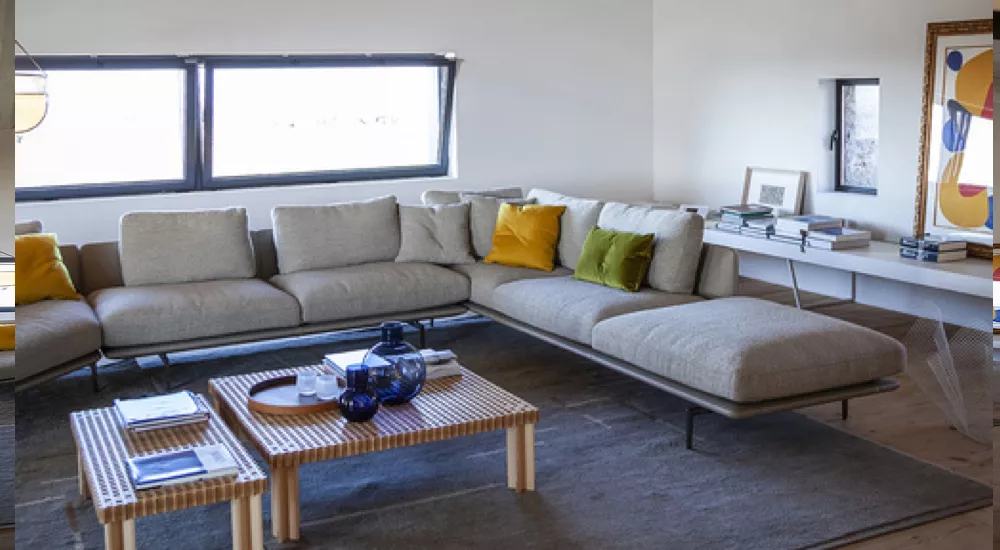 Poltrona Frau Get Back Sofa in Grau mit gelben Kissen, modernes Wohnzimmer, Holztisch, Bücher und Kunst im Hintergrund.