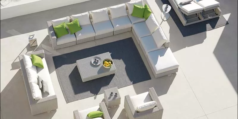 Ethimo Cube Outdoor-Sofa in Weiß mit grünen Kissen, auf einer Terrasse mit grauem Teppich und Beistelltisch, Vogelperspektive.