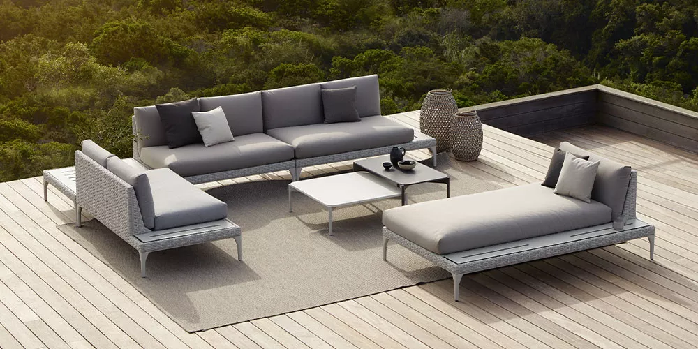 Dedon Loungesofa Mu auf einer Terrasse mit Blick auf grüne Landschaft mit Kissen und Beistelltisch in einer entspannten Atmosphäre