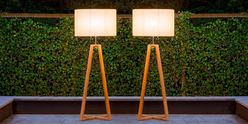 Zwei Royal Botania Club Gartenleuchten mit Holzgestell und cremefarbenem Schirm vor einer grünen Hecke bei Dämmerung.