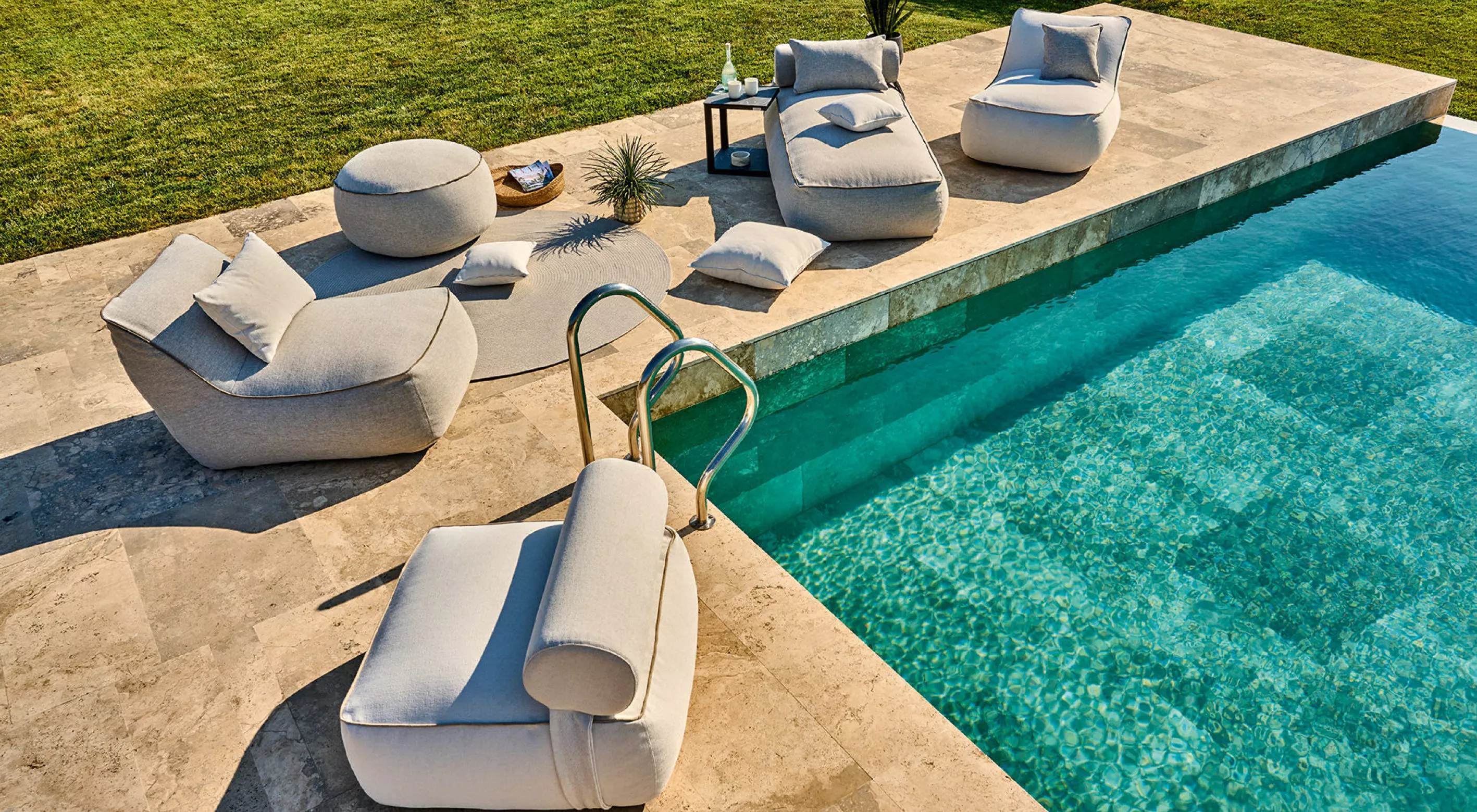 Maliha Lounge-Set in Pebble Cream mit Sessel, Hocker und Kissen auf einem Taupe-Teppich am Pool, Gartenmöbel in entspannter Atmosphäre.