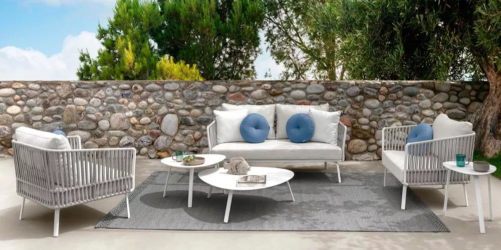 Talenti Milo Lounge Outdoor-Loungemöbel in Weiß und Grau auf einer Terrasse mit Steinmauer im Hintergrund, stimmungsvolle Gartenatmosphäre.