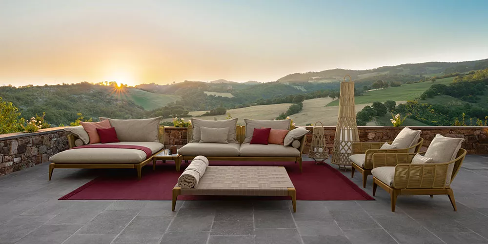 Talenti Kollektion Cruise Teak Lounge-Set in Naturtönen auf einer Terrasse mit Blick auf eine malerische Landschaft bei Sonnenuntergang.