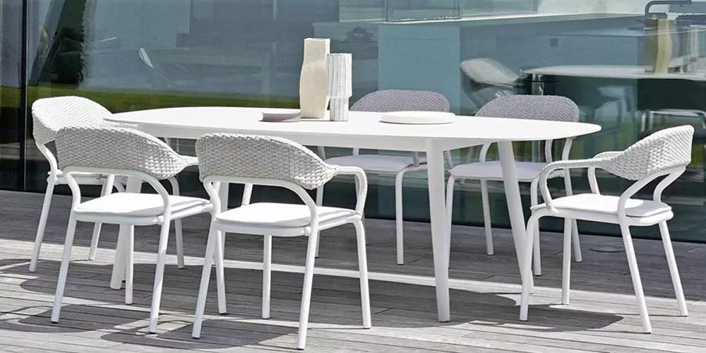 Varaschin Ellisse Essgruppe in Weiß auf einer Terrasse, bestehend aus einem ovalen Tisch und sechs Stühlen, vor einer Glasfassade.