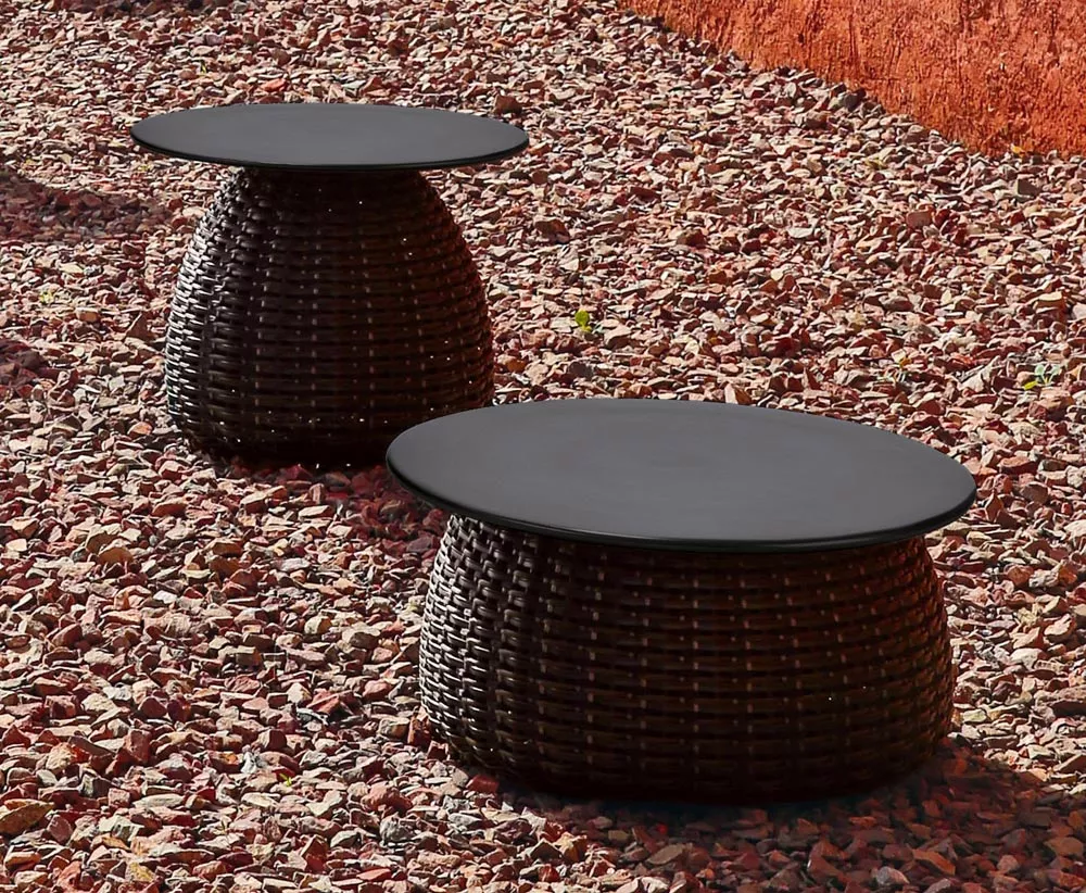 Dedon Porcini Beistelltisch in einem Garten auf Kieselsteinen platziert im Hintergrund eine rote Wand