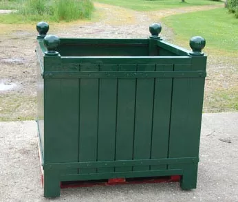 Orangerie Pflanzkübel aus lackiertem Akazienholz steht auf einer Palette im Freien auf einem Betonboden mit Gras im Hintergrund