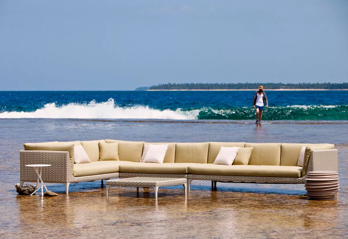 Dedon Mu Kollektion Outdoor Gartenmöbel in Strandumgebung mit Wellen im Hintergrund und einer Person die am Wasser entlangläuft