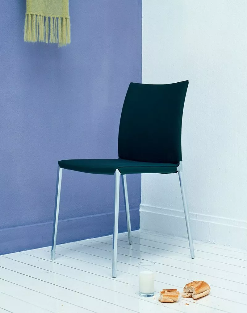 Ein Zanotta Lia Stuhl steht in einer Ecke auf weißem Boden neben einem Glas Milch und zerbrochenem Gebäck vor einer blauen Wand.