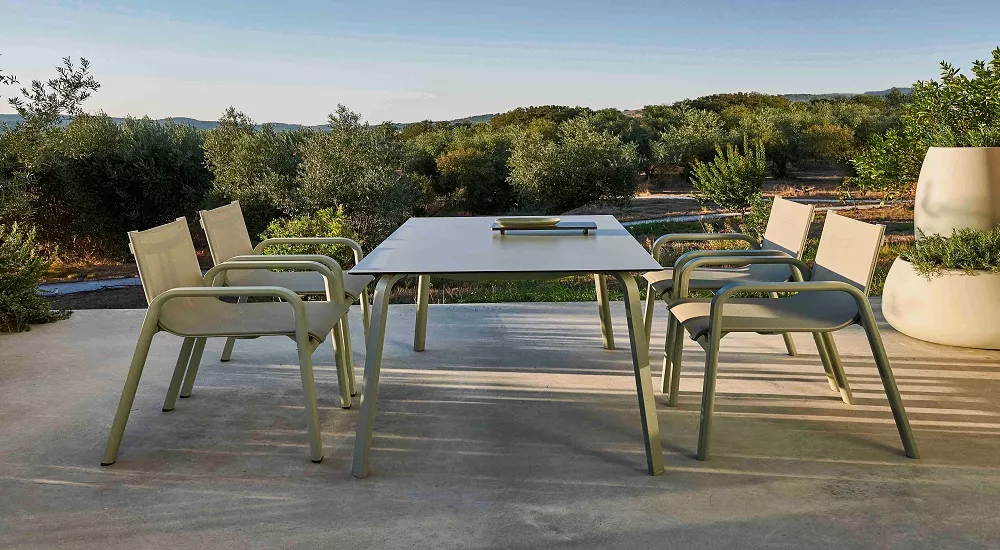 Grau zementfarbener Dining Club Armchair und Dining Table 160 von Stack auf einer Terrasse mit Blick auf eine grüne Landschaft.