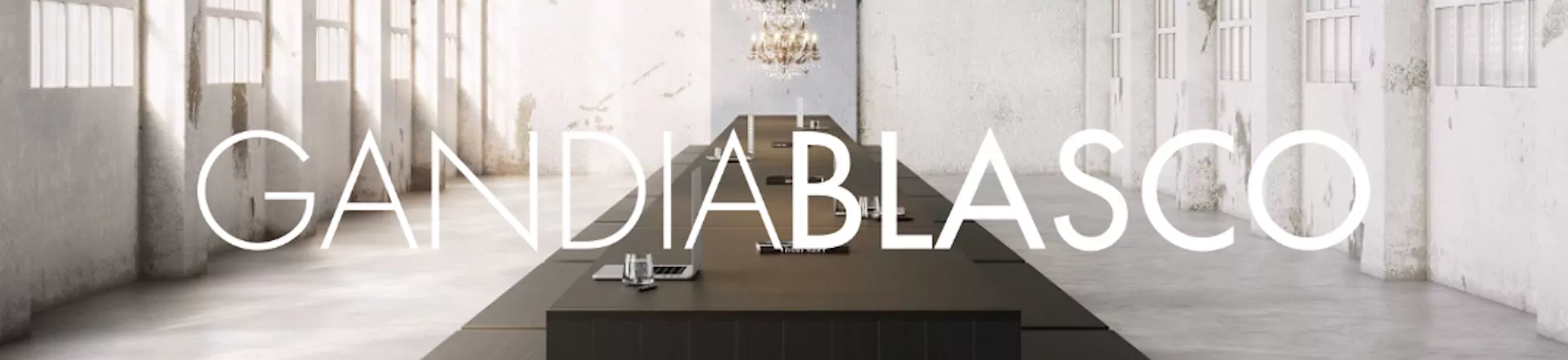 Banner mit Gandia Blasco Logo vor einem modernen, minimalistischen Raum mit großen Fenstern und einem langen Tisch in neutralen Farben.