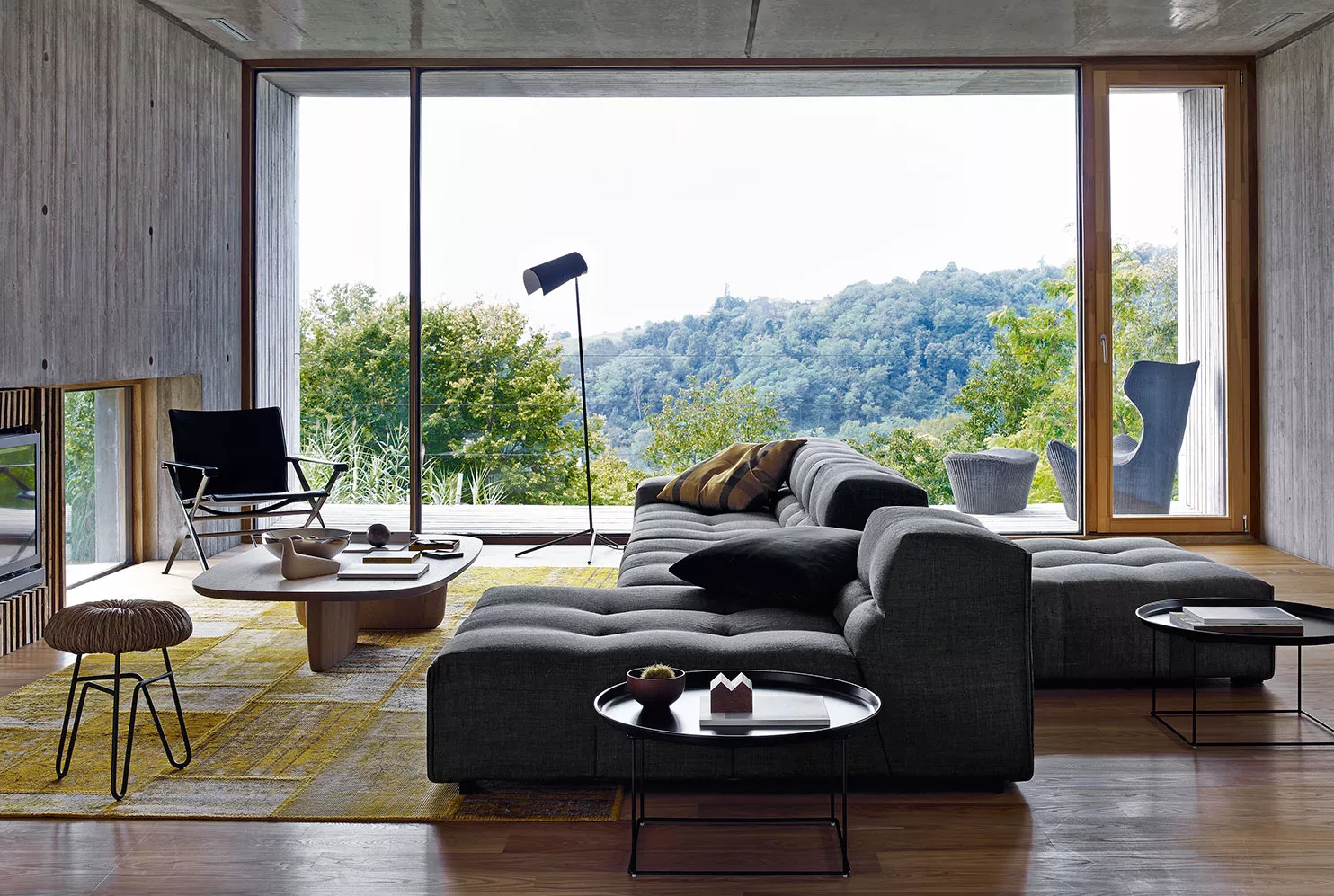 B&B Italia Tobi-Ishi Couchtisch in hellem Holz vor einem grauen Sofa in einem modernen Wohnzimmer mit Panoramablick auf die Natur.