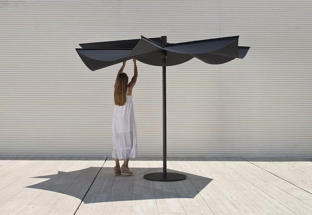 Frau in weißem Kleid richtet den Calma OM Sonnenschirm aus eloxiertem Aluminium mit 300 cm Durchmesser vor einer weißen Wand aus.