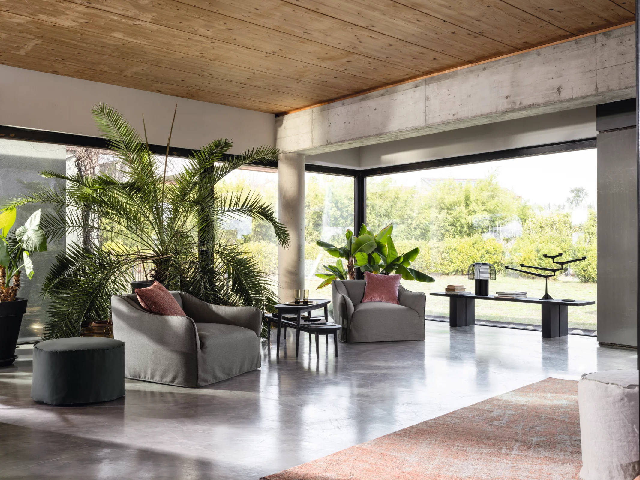 Zwei Gervasoni Sofas mit roten Kissen stehen in einem modernen Wohnzimmer mit großen Fenstern und Pflanzen im Hintergrund.