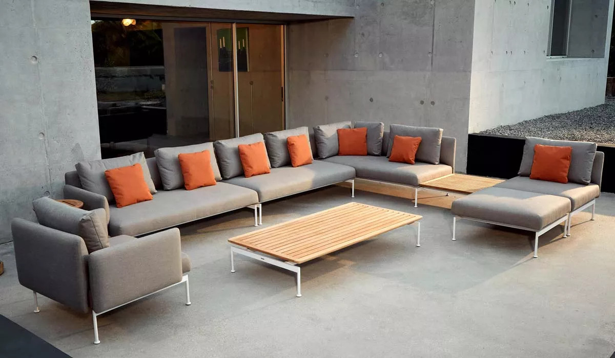 Barlow Tyrie Layout Loungegruppe in Grau mit orangefarbenen Kissen auf einer modernen Terrasse vor einer Betonwand.