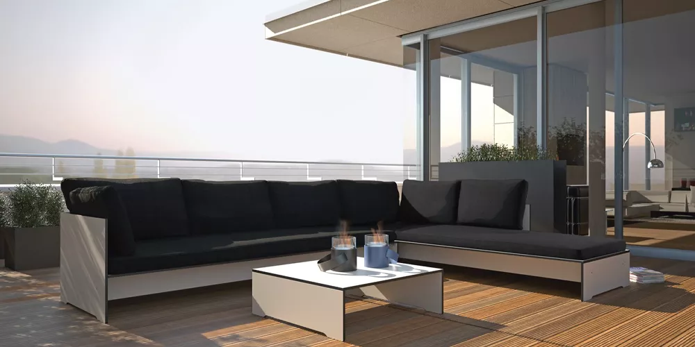 Conmoto Kollektion Riva, schwarzes Outdoor-Sofa auf moderner Terrasse mit Holzboden und Glasgeländer, stimmungsvolle Abendbeleuchtung.