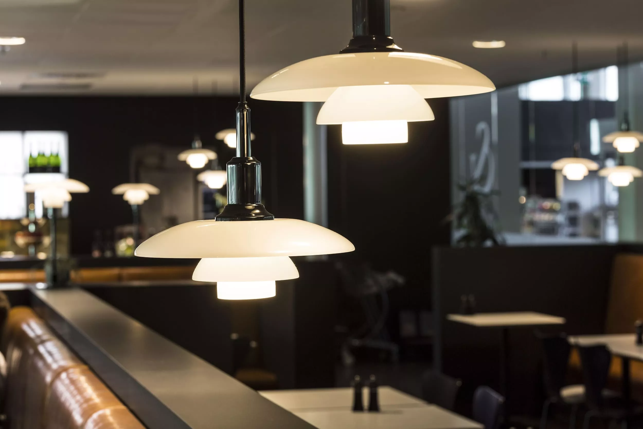 Hängelampe Louis Poulsen PH 3/2 in Weiß, beleuchtet, in modernem Café-Ambiente mit dunklem Hintergrund.