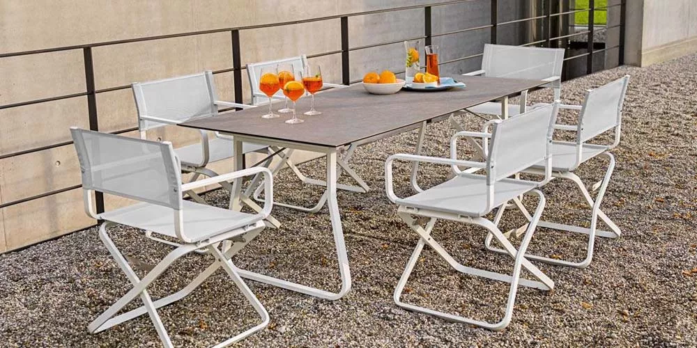 Weißhäupl Ahoi Gartenmöbel-Set in Weiß auf Kiesboden mit gedecktem Tisch und Getränken, vor einer modernen Betonwand.