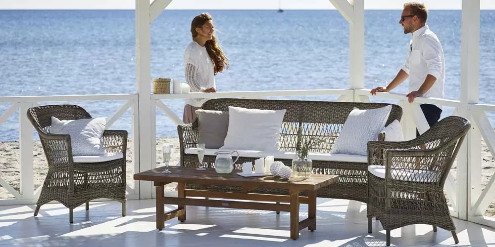 Sika-Design Charlot Loungegruppe in Grau auf einer Terrasse am Meer, bestehend aus Sofa, Sesseln und Tisch, in entspannter Sommeratmosphäre.