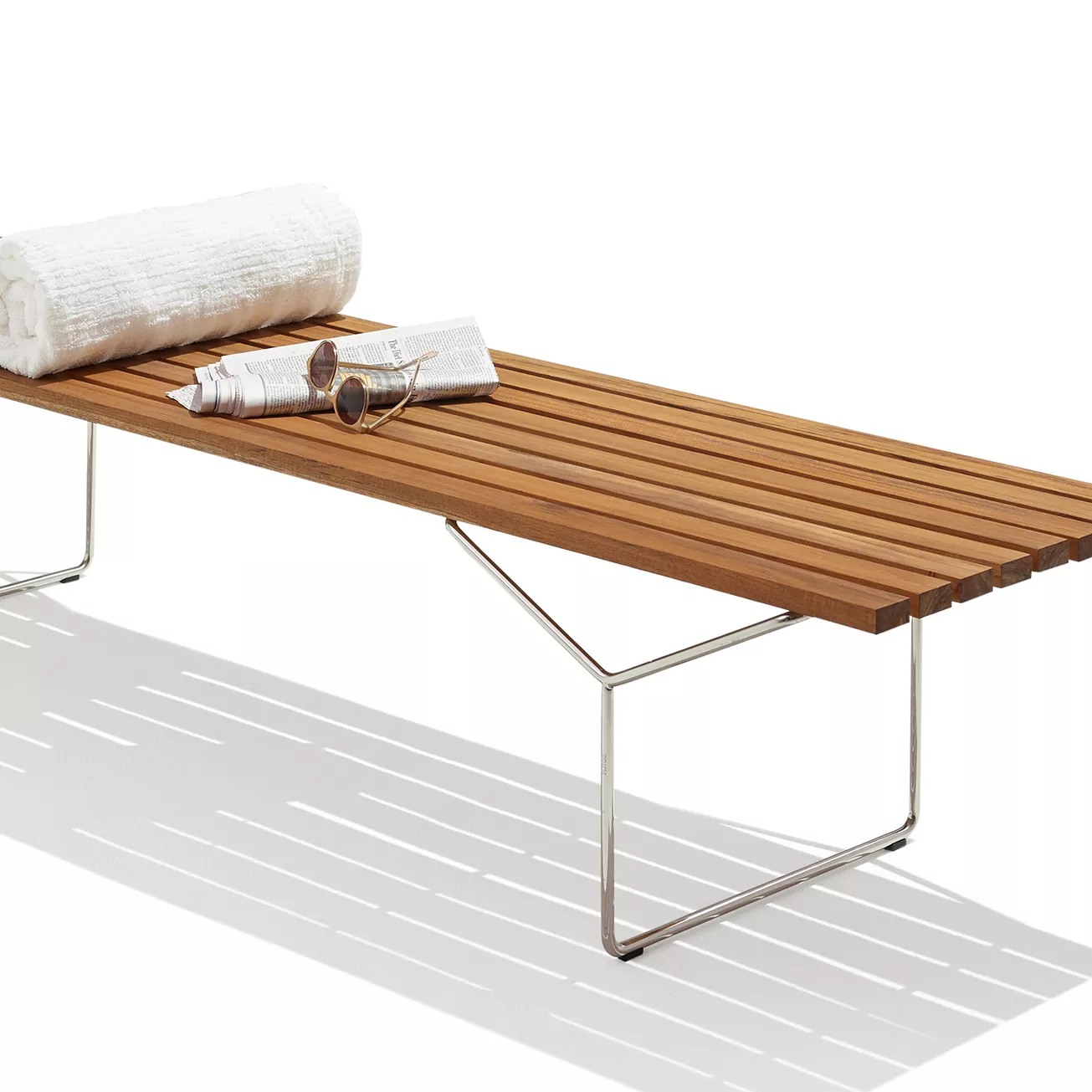 Knoll Harry Bertoia Lattenbank Teak mit Handtuch und Zeitschriften auf einer weißen Oberfläche ohne Hintergrund