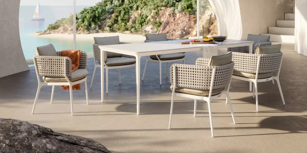 Dedon Endless Ocean Bellmonde Dining Set auf einer Terrasse mit Blick auf das Meer und eine grüne Insel im Hintergrund