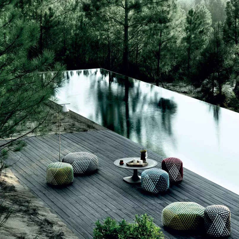 B&B Italia Tramae kleiner Hocker in verschiedenen Farben auf einer Terrasse neben einem Pool in einer Waldlandschaft mit Getränken auf einem Tisch