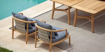 Zwei Poltrona Frau Secret Garden Stühle in hellem Holz und grauem Stoff auf einer Terrasse am Pool, stimmungsvolles Outdoor-Setting.