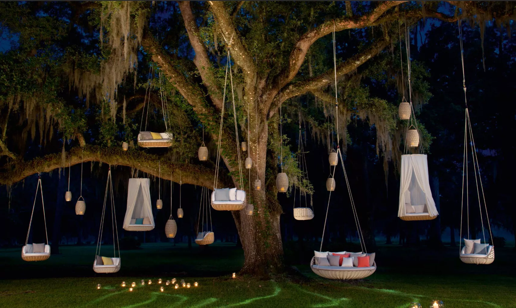 Dedon Swingrest Hängesessel und Hängesofas hängen an einem großen Baum bei Nacht umgeben von Kerzenlicht in einer stimmungsvollen Atmosphäre