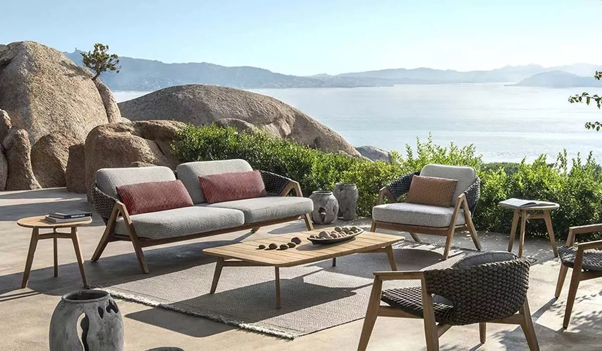 Ethimo Knit Outdoor Loungegruppe in Grau und Holz auf einer Terrasse mit Meerblick und Felsen im Hintergrund.