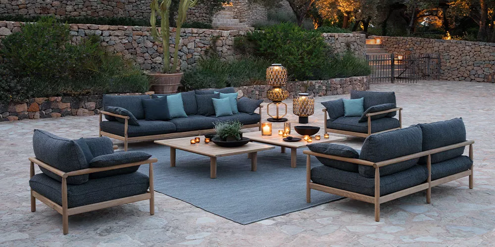 Dedon Tibbo Kollektion Gartenmöbel auf einer Terrasse mit Steinboden und Pflanzen im Hintergrund stimmungsvolle Beleuchtung durch Laternen und Kerzen